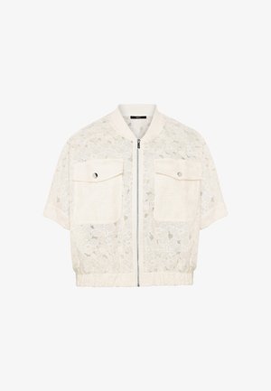 Veste blanche en dentelle à manches courtes avec fermeture éclair à l'avant et deux grandes poches à rabat avec boutons, taille élastiquée et col côtelé.