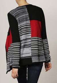 Maglione lavorato a maglia nero, rosso e grigio con maniche oversize. Presenta motivi a trama variata e una forma squadrata. Finitura liscia, vestibilità comoda.