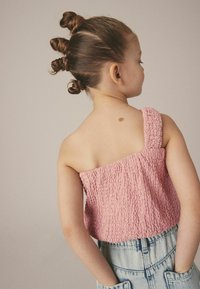 Vaaleanpunainen, teksturoitu crop-top, jossa on yksi olkaimestrappi, yhdistettynä korkeavyötäröisiin farkkushortseihin, joissa on etutaskut ja haalistunut pinta.