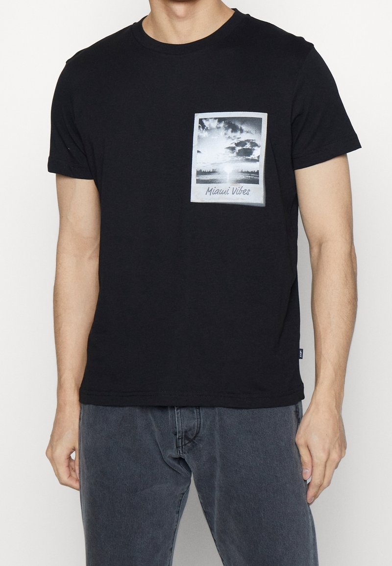 T-shirt in cotone nero con design della tasca grafica rettangolare che presenta una scena di Miami in bianco e nero e l'etichetta testuale "Miami Vibes."