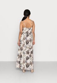 Maxi šaty s tenkými ramínky, s květinovým a listovým vzorem v béžové, hnědé a zelené barvě. Materiál se zdá být lehký a splývavý.