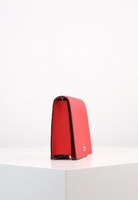 Borsa a mano in pelle rossa con forma strutturata, dotata di bordi neri e un accento logo discreto alla base. Texture liscia e design moderno.