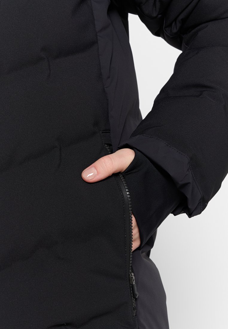 Giacca a vento nera con finitura testurizzata, dotata di tasca con zip e polsini elasticizzati. Il materiale sembra spesso e isolato.