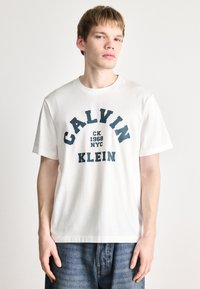 Valge puuvillane T-särk ümmarguse kaelusega. Peal on julged tumesinised kirjad: "CALVIN KLEIN CK 1968 NYC" kaarekujulises disainis. Loodud vabaks istuvuseks.