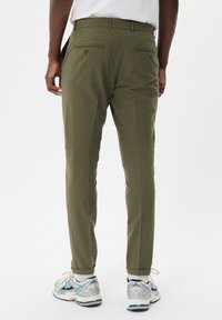 Pantalones verde oliva con un corte ajustado, que cuentan con bolsillos laterales, dos bolsillos traseros con detalles de botones y una textura suave. Combinados con zapatillas grises.