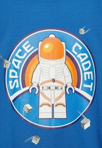 Modré tričko s grafikou astronauta v oranžové helmě, obklopeného šedými kostkami a textem "VESMÍRNÝ KADETI".