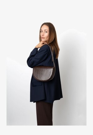 Brun læder skuldertaske med en buet silhuet, tekstureret overflade og en bred rem. Båret over skulderen mod en simpel baggrund.