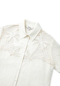 Bílá košile s límečkem, předním zapínáním na knoflíky a propracovanou vyšívkou s palmovými vzory na průhledné tkanině.