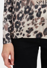 Beige en zwarte luipaardprint top met lange mouwen en een slouchy pasvorm. Bevat een decoratieve patch met stenen-details aan de voorkant.