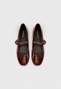 Brown patent leather Mary Jane shoes with a square toe, flat heel, and a thin strap featuring a metal buckle. Black insoles visible inside.