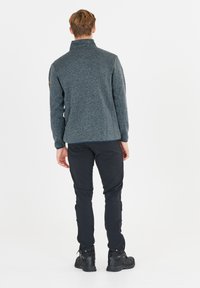 Grå fleecejacka med dragkedja och hög krage, texturerat tyg och kontrasterande marinblå detaljer, i kombination med svarta byxor och robusta svarta kängor.