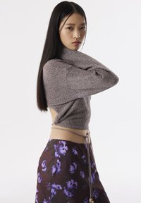Haut crop enbrown ajusté avec un col montant et des côtés ouverts, associé à une jupe à motifs floraux violette avec une taille à cordon.
