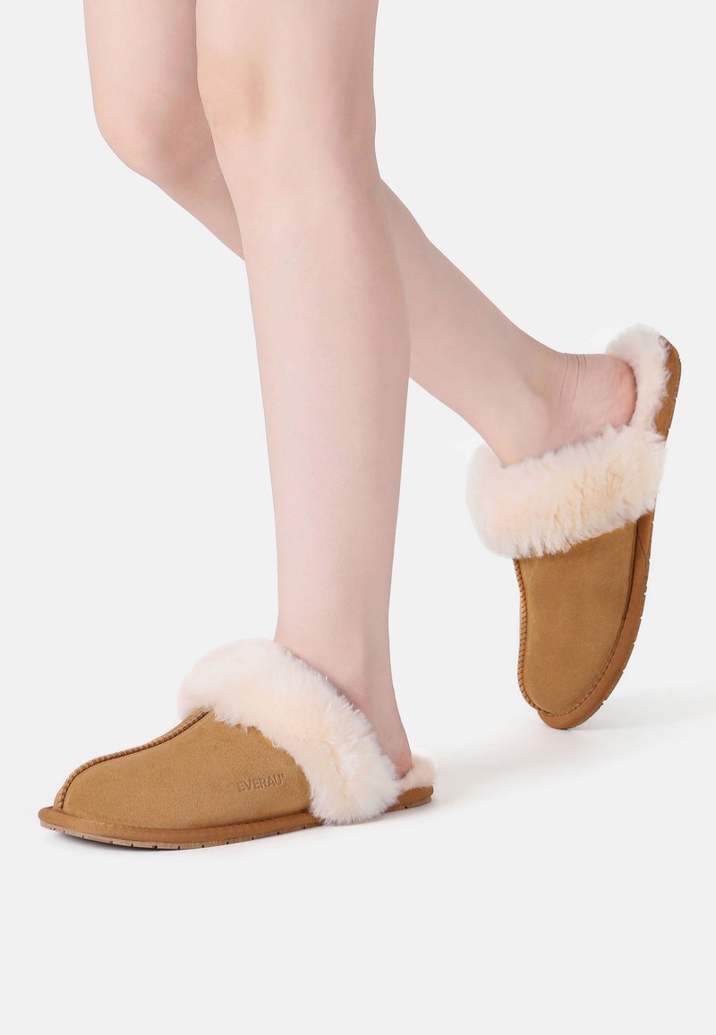 Tan suede slippers with a fluffy, light beige fur lining. Open-toe design, soft texture, and a flexible sole for comfort.