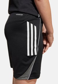 Bermudas deportivas negras hechas de un tejido transpirable, con un diseño de tres rayas blancas, corte ajustado y sutiles detalles en los paneles laterales.