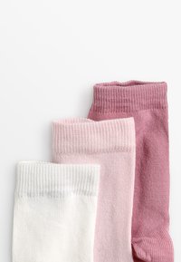 Tre par sokker i hvit, lys rosa og mørk rosa. Laget av ribbet materiale med elastiske topper og glatt tekstur.