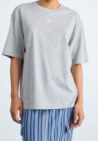 T-shirt in cotone grigio con colletto tondo e maniche corte. Presenta un piccolo logo Adidas bianco sul petto. Tessuto morbido, vestibilità rilassata.