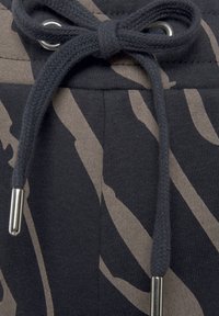 Tkanina mikiny s černo-béžovými pruhy, zdobená pleteným šňůrkovým stahovadlem s kovovými koncovkami a žebrovaným výstřihem.