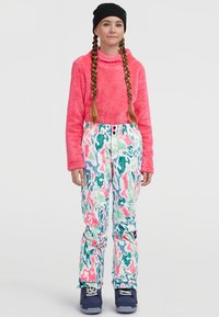 Suéter rosa difuso con alto cuello, combinado con pantalones de nieve multicolor y estampados. Botas de esquí azules completan el atuendo de invierno.