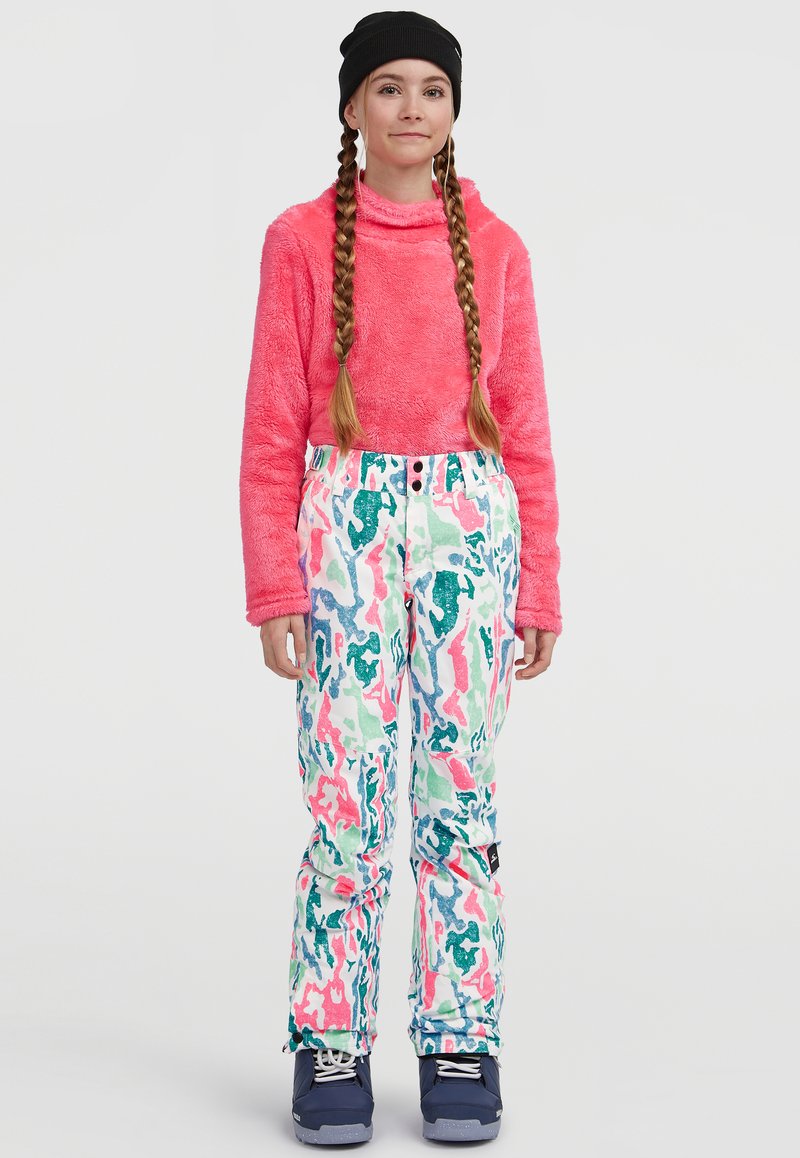 Suéter rosa difuso con alto cuello, combinado con pantalones de nieve multicolor y estampados. Botas de esquí azules completan el atuendo de invierno.