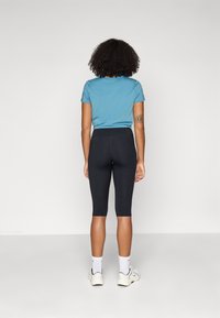 T-shirt ajusté bleu clair et leggings capri noirs, présentés de dos, avec des textures unies et des couleurs contrastantes, associés à des chaussettes et des chaussures blanches.