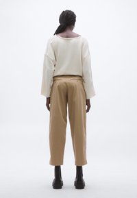 Krém színű pulóver nyers szegélyű nyakkivágással és hosszú ujjakkal, hozzá párosítva világosbarna, széles szárú nadrág, hátul zsebekkel. Fekete platform csizmák.