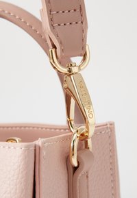 Pink leather handbag strap with gold hardware, featuring a snap hook and contrasting stitching. Textured surface detail visible.
