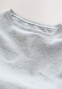 Tela gris claro con canalé y cuello redondo, mostrando la textura y los detalles de costura del cuello de la camisa.