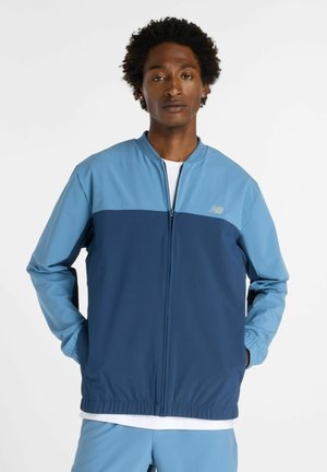 Chaqueta de cremallera en azul marino y azul claro con cuello alto, puños elásticos y un diseño liso. Presenta un pequeño logo en el pecho.