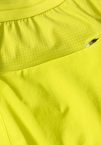 Heldergele sporttop met een soepele textuur, voorzien van een gaaspaneel in een ruitpatroon bij de halslijn en een klein ritsdetail.
