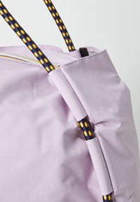 Licht paarse tas met geweven zwarte en gele banden, met een gladde textuur en geplooid ontwerp aan de bovenkant. Ritssluiting detail.