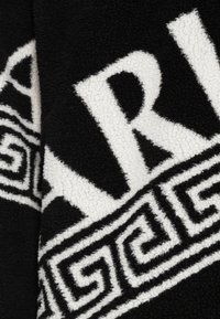 Black and white fleece fabric with plush texture. Features bold lettering and a Greek key pattern along the bottom edge.
