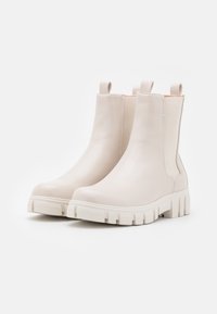 Białe skórzane botki sięgające kostki z masywną gumową podeszwą, z elastycznymi panelami bocznymi i pętlami umożliwiającymi łatwe zakładanie. Gładka tekstura i minimalistyczny design.