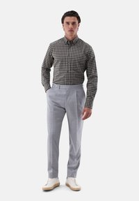 Karierte, dunkelgrüne und weiße Hemdbluse, kombiniert mit hellgrauen Hosen; das Model steht in weißen Sneakers und präsentiert eine moderne Passform.