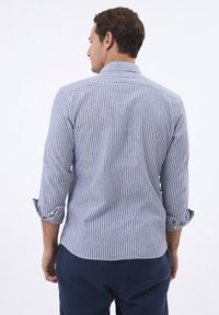 Camisa de hombre a rayas azules y blancas, con mangas largas, puños enrollados, cuello puntiagudo y dobladillo curvado, fabricada con un tejido ligero.