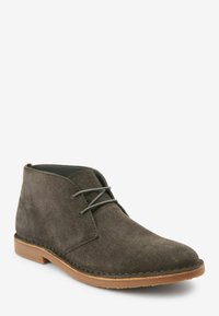 Botas desierto de ante en gris oscuro con punta redondeada, diseño de cordones y una suela de goma marrón ligera. Superficie texturizada con detalles de costura.