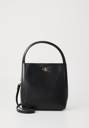 Bolso de mano de piel negra con un asa redondeada, acento de logo dorado y correa para el hombro desmontable. Textura suave y forma estructurada.