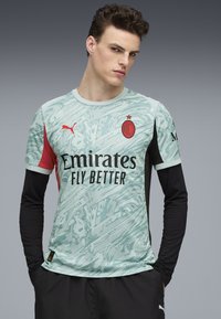 Puma AC Milan -paita, jossa on mintunvihreä pohja, abstrakteja kuvioita, mustat hihat, punaiset yksityiskohdat ja musta teksti "Emirates Fly Better."
