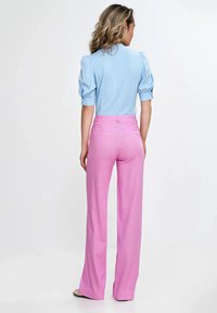 Jasnoniebieska bluzka z bufkami w połączeniu z różowymi spodniami z wysokim stanem i rozszerzanymi nogawkami. Gładki materiał o subtelnym połysku i dopasowany krój.