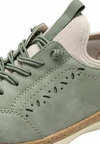 Baskets en daim vert avec un accent texturé beige, lacets ronds et perforations décoratives sur le côté. Semelle en caoutchouc avec texture légère.