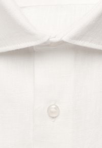 Gros plan sur le col d'une chemise blanche avec un bouton transparent unique fermé sur un tissu texturé.