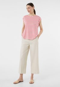 Różowo-biała prążkowana bluzka z krótkim rękawem i okrągłym dekoltem, zestawiona z beżowymi spodniami o szerokich nogawkach oraz plecionymi sandałami wsuwanymi.