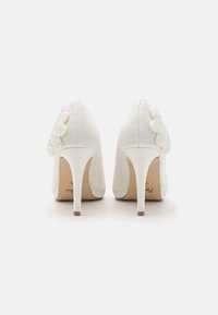 Bílé lodičky na vysokém podpatku s hladkým textilním povrchem a perlovým akcentem na zadní straně. Elegantní stiletto design.