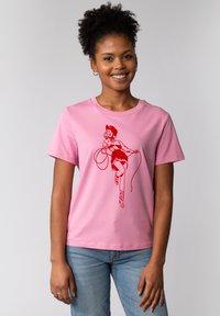 Roze katoenen t-shirt met een rode afbeelding van een persoon met een lasso, korte rok en cowboylaarzen. Ronde halslijn en korte mouwen.