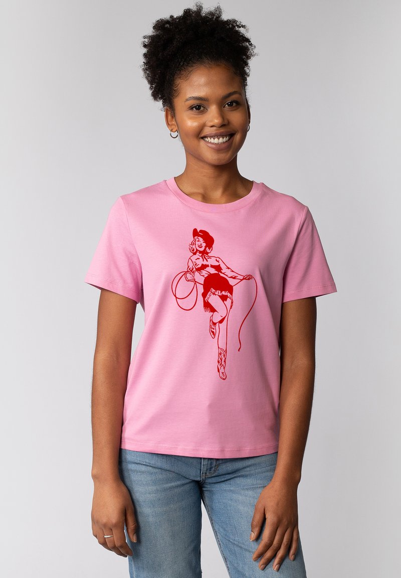 Roze katoenen t-shirt met een rode afbeelding van een persoon met een lasso, korte rok en cowboylaarzen. Ronde halslijn en korte mouwen.