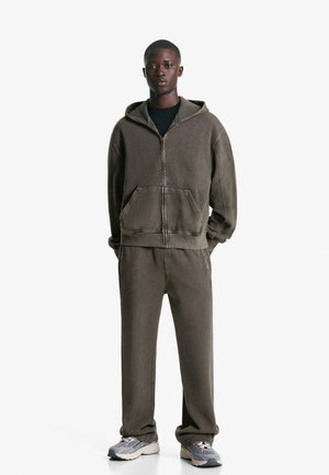 Hooded zip-up sweatshirt and matching pants in a muted olive color. Fabric has a soft, textured appearance. Worn with gray sneakers.