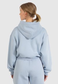 Felpa azzurra chiara con cappuccio, vestibilità ampia e polsini a costine. Tessuto morbido, senza motivi o dettagli visibili. Design semplice.