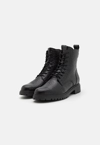 Bottines en cuir noir avec une surface texturée, un design à lacets et des semelles en caoutchouc robustes avec un léger talon et une languette.