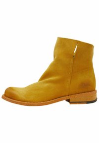 Bota de ante a la altura del tobillo en color mostaza con un diseño de lado abierto, punta redondeada y un tacón apilado en un tono marrón claro contrastante.