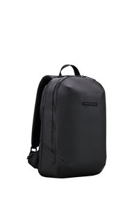 Sac à dos noir avec une finition lisse et mate, une forme courbée et des bretelles rembourrées. Il comprend une poignée supérieure et une poche zippée sur le côté.