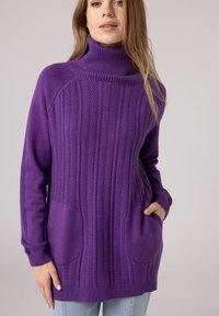 Maglione lavorato a maglia di colore viola con colletto alto, caratterizzato da un motivo a trecce, polsini a costine e due tasche frontali. Texture morbida.